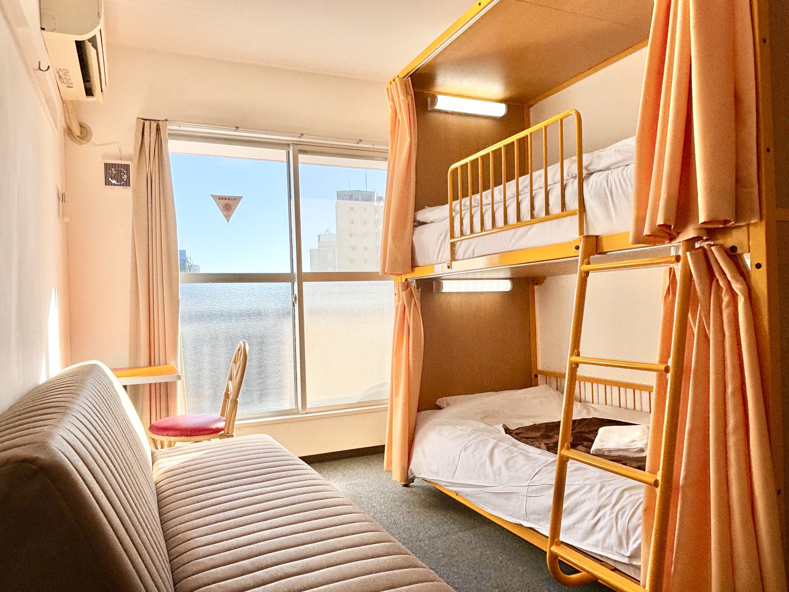 “Bright and clean dormitory-style room with bunk beds and sofa at Sakura Hotel Nippori in central Tokyo, offering affordable stay for groups and travelers”